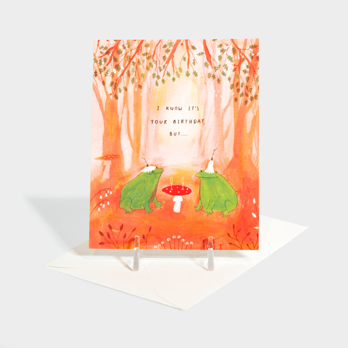 Greeting card with two frogs sitting by a mushroom table with champagne glasses.