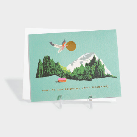 Greeting card with an illustration of a mountain and forest. A goose flies in front of the sun. Features gold foil-stamped  text and details. 