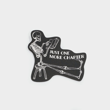 Black sticker with white ink skeleton reading a book. Text reads, "Just one more chapter".