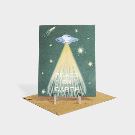 Greeting card with a UFO illustration and "peace on earth" appearing to abducted.