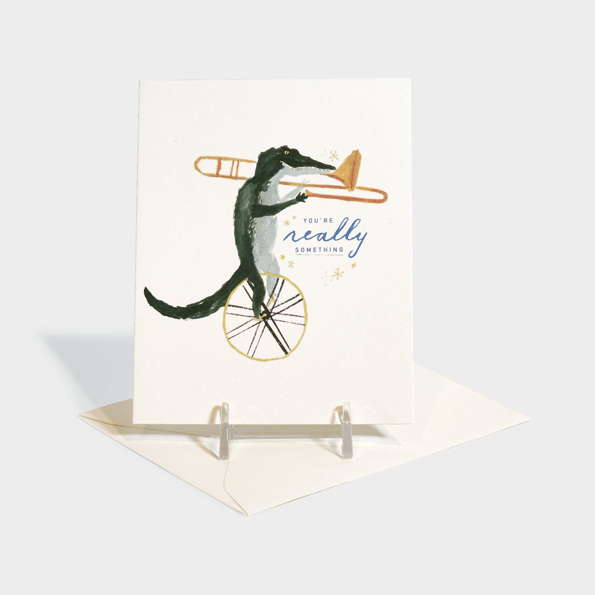 Greeting card with an illustration of an alligator riding a unicycle playing the trumpet.